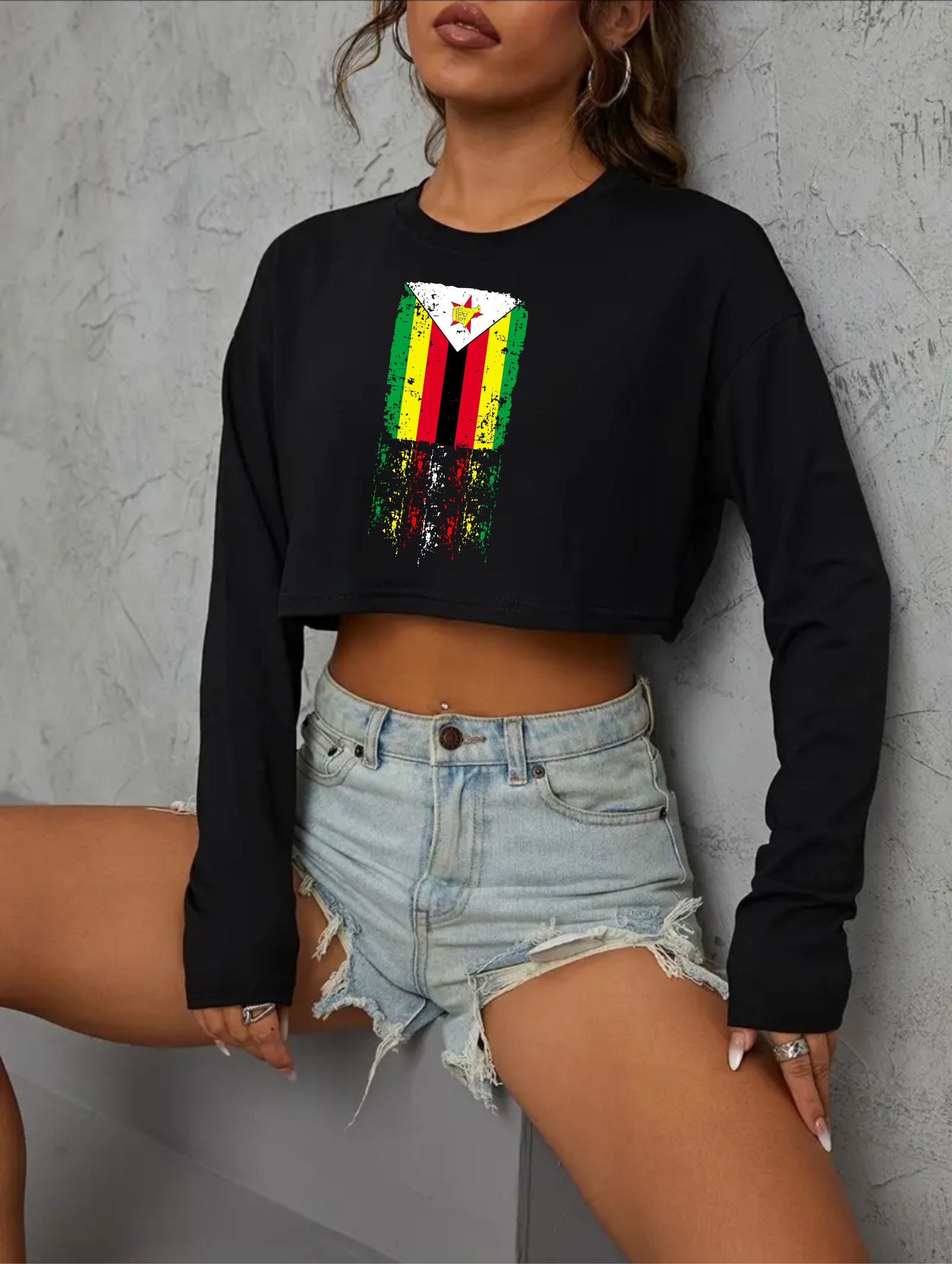 Person wearing a black cropped sweatshirt with a colorful graphic design and denim shorts against a gray background